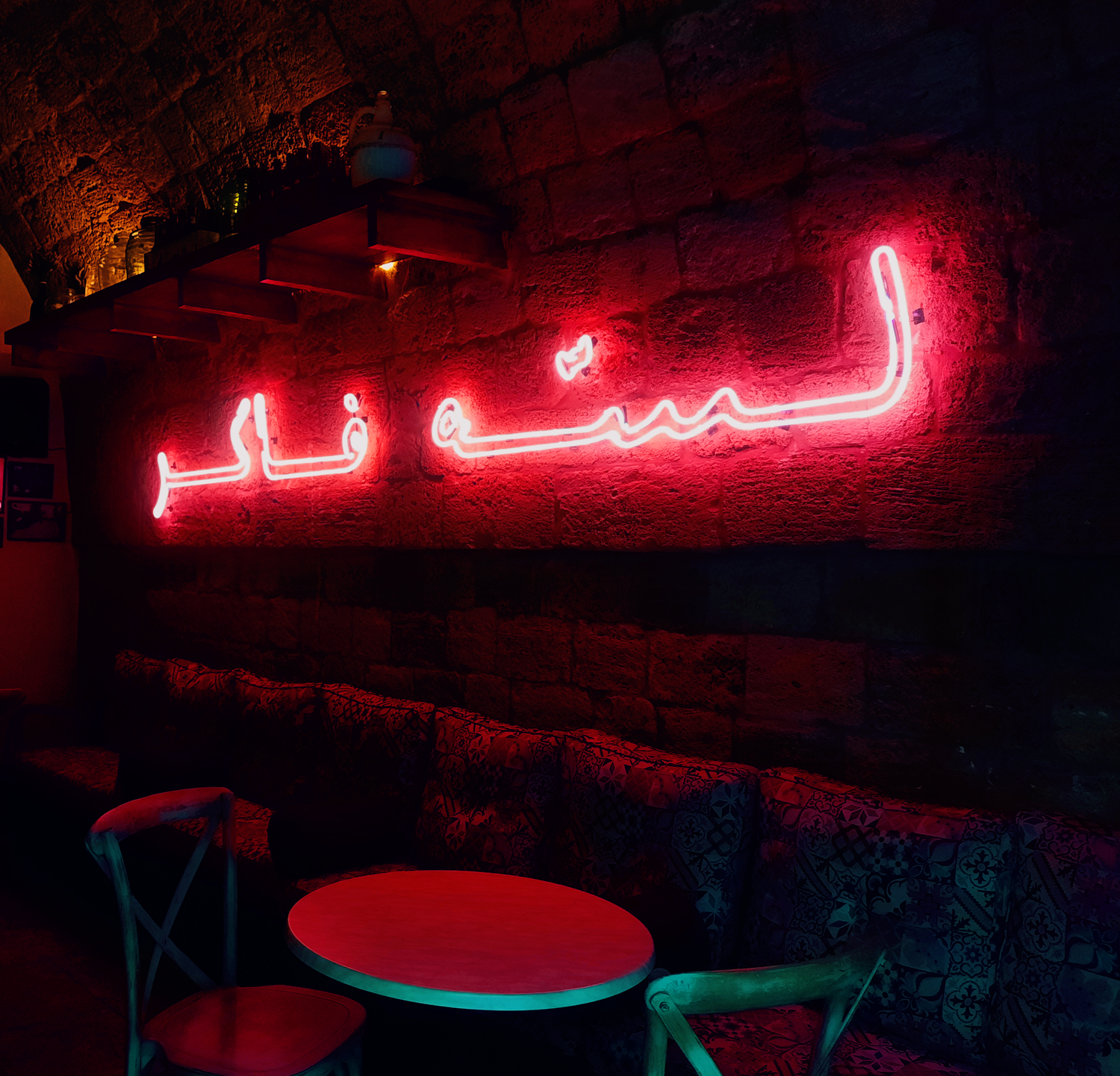Neon sign with Arabic text on a stone wall in a dimly lit room.